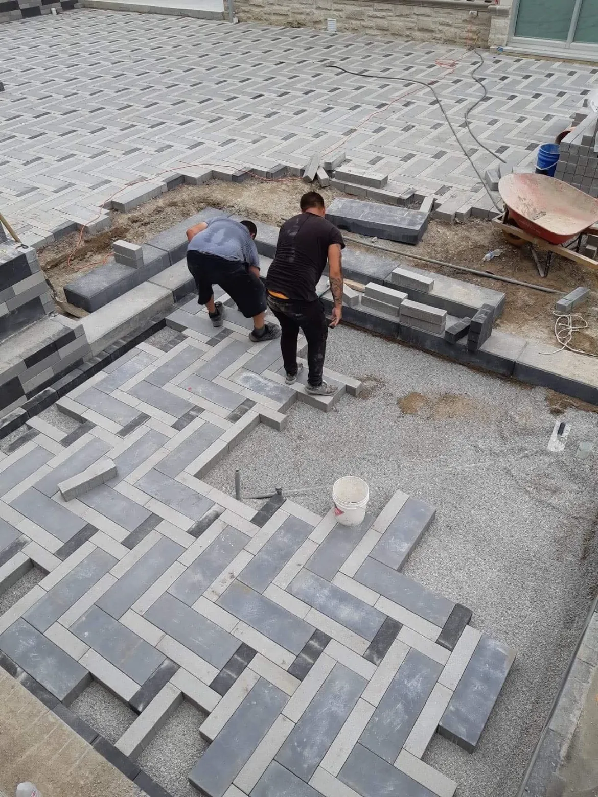 Two installers laying a grey and charcoal herringbone paver patio